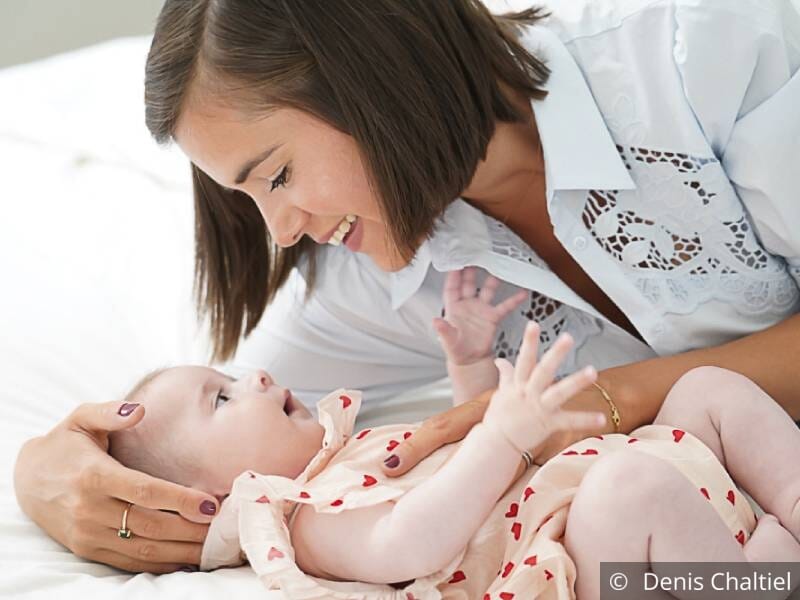 Une maman allongée à côté de son bébé et qui lui sourit.